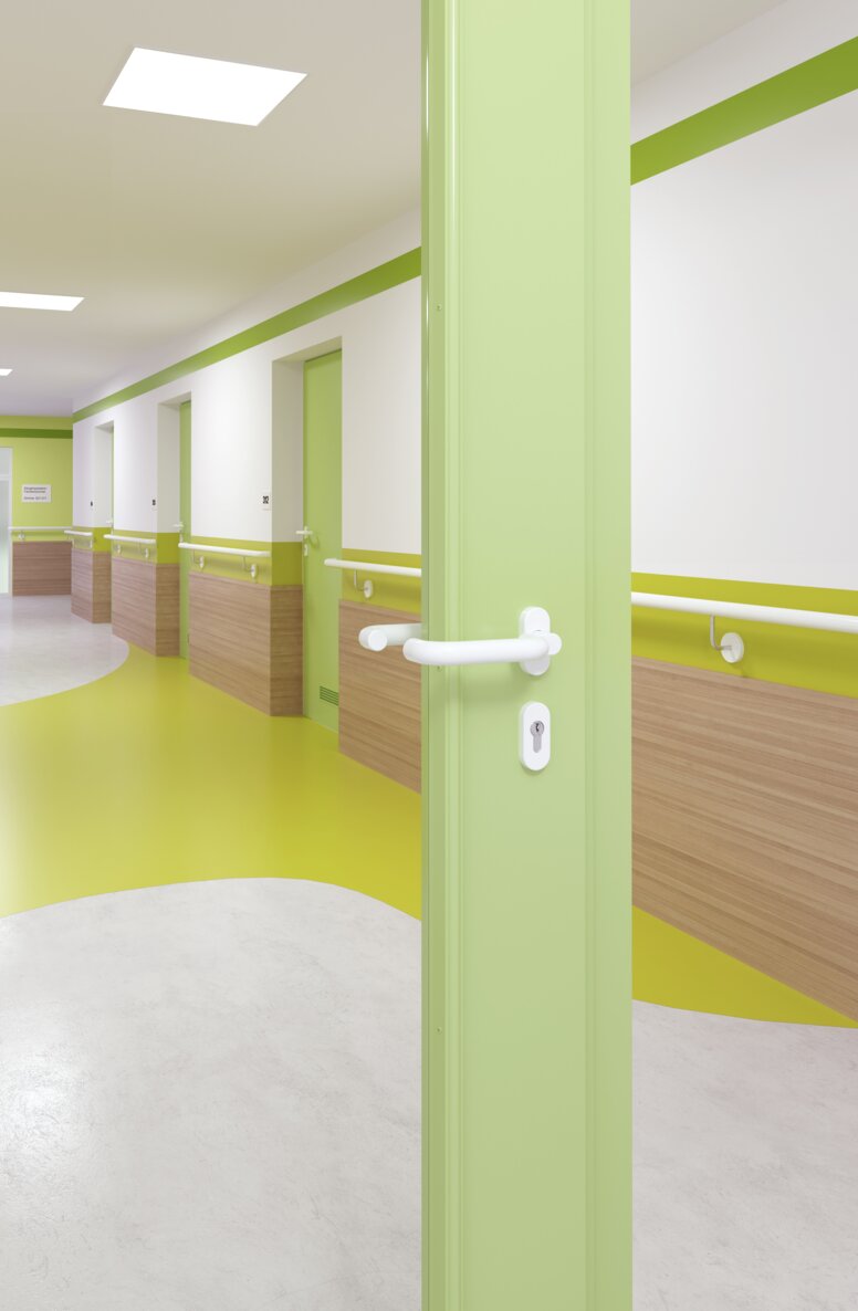 Verglaste Krankenhaustür mit grünem Rahmen ausgestattet mit einem Türgriff in der Farbe Signalweiß aus Polyamid